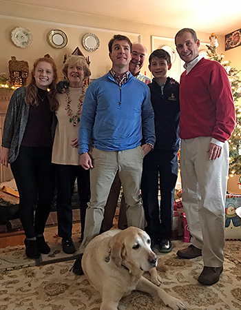 At Pat's parent's house, Galahad enjoys time with his family in front of a lit Christmas tree. Presents can be seen under the tree and the happy bunch looks festive.