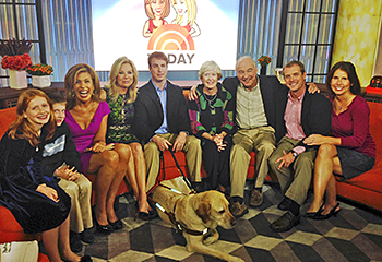 Pat and his family sit on a bright red couch with the hosts of the Today show as they get ready to appear before a national audience. Galahad, on the carpet in front of them, is unphased by the cameras.