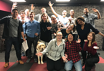 In the fall of 2019, Pat and fourteen graduating classmates stand on a small stage in the basement lounge at DC Improv. Hogan looks focused as he plays the role of working dog amidst the laughter.